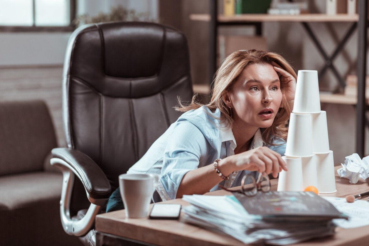 Женщина строит пирамиду из бумажных стаканчиков на рабочем столе