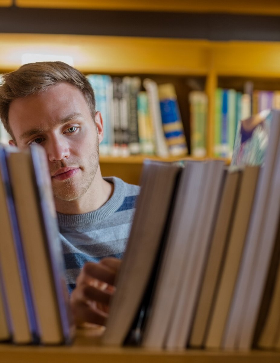 Мужчина рассматривает книги на полке